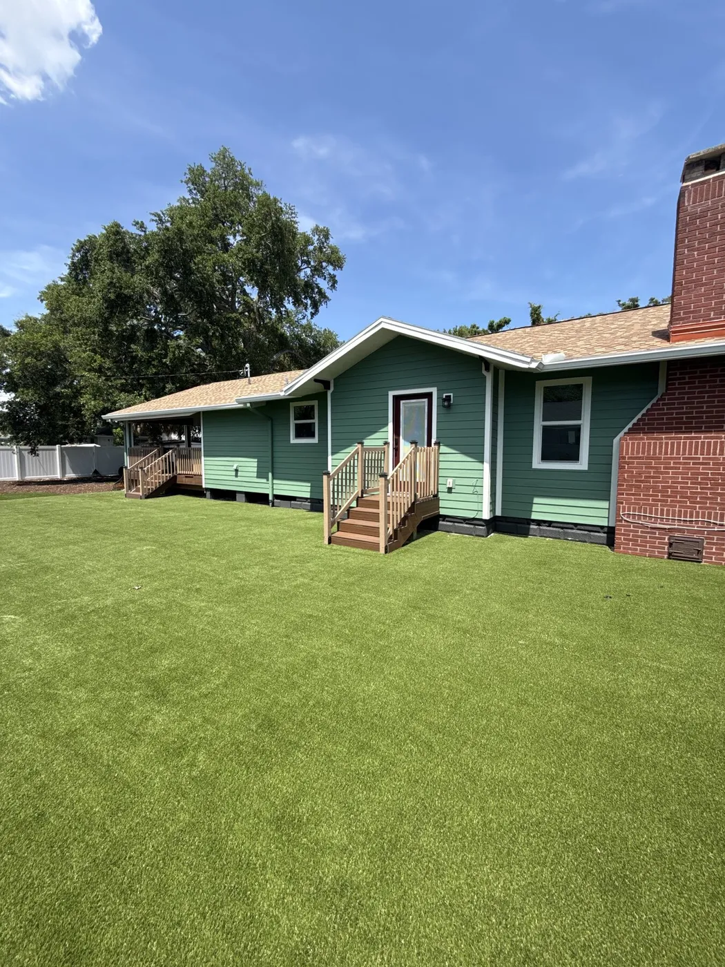 Full backyard of artificial turf behind a green cottage-style home