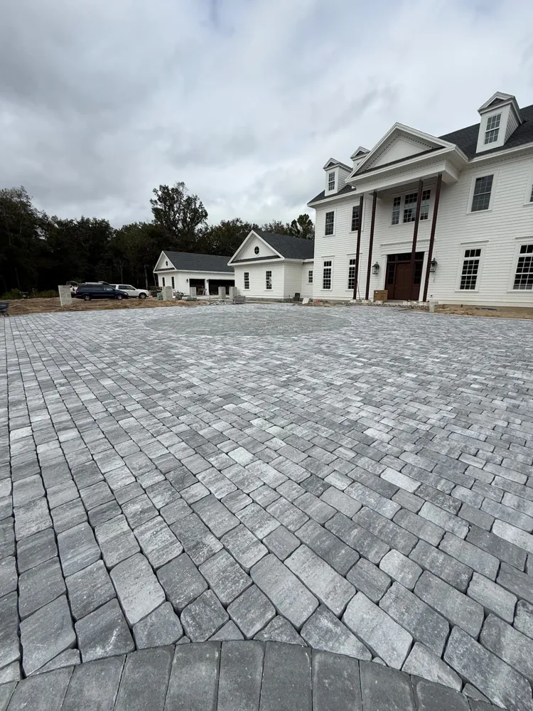 Gray cobblestone paver motor court in front of a large white home