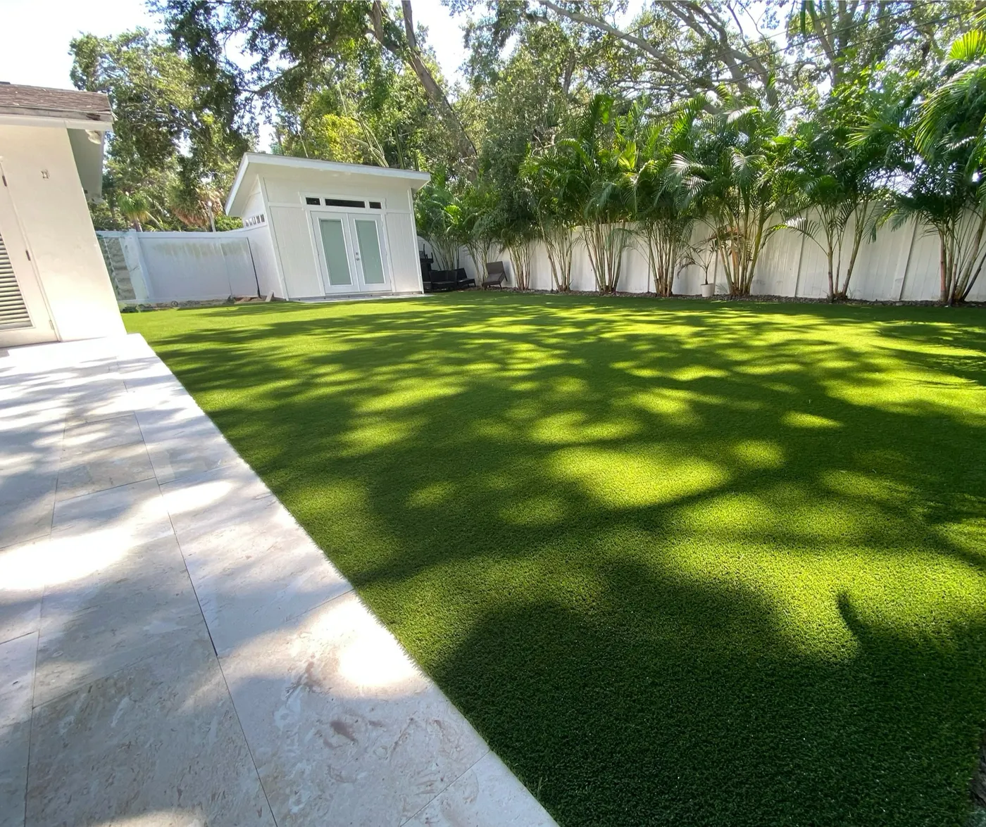 Wide backyard lawn of new artificial turf beside a paved walkway with palms behind