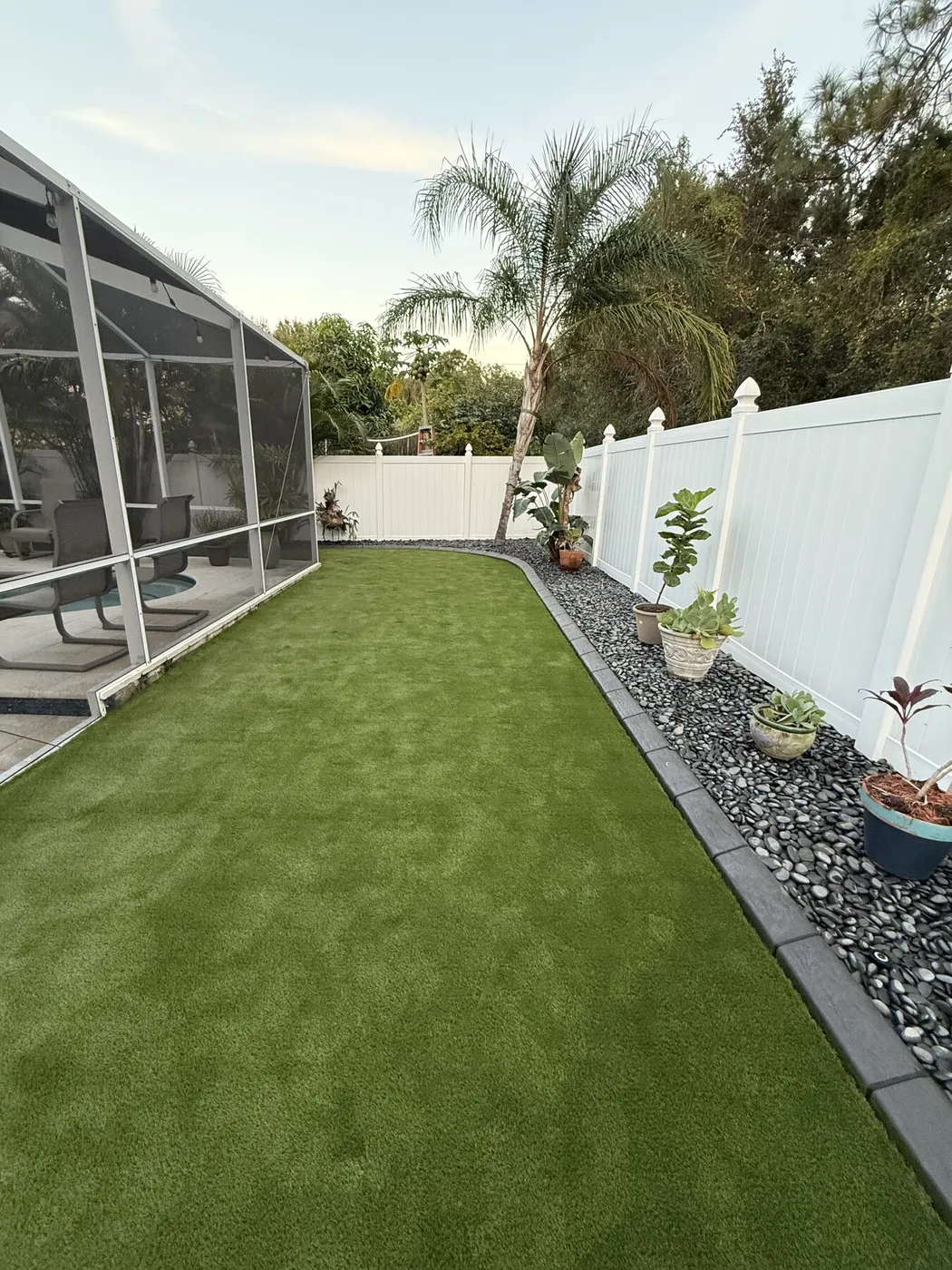 Turf run along a screened lanai with a river rock border and white fence